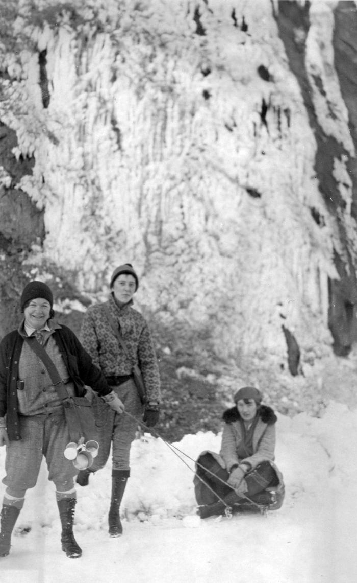 Two women standing in snow pulling a third on a sled