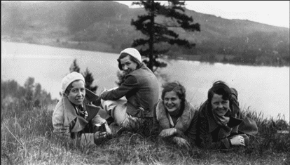 Four women on a grassy hill overlooking a lake