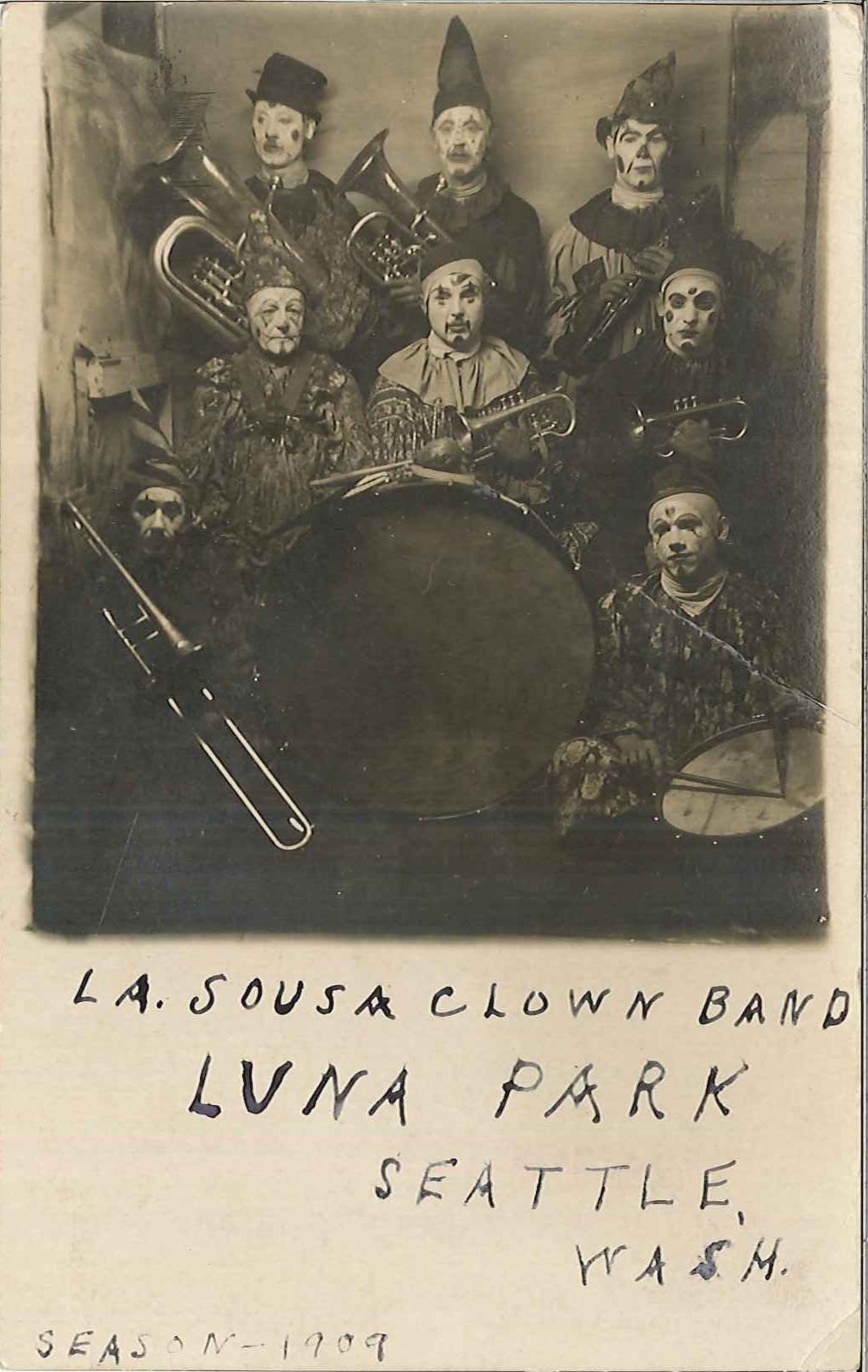 1909 postcard showing 8 musicians made up as clowns posing with their instruments. Writing on the card says: "La Sousa Clown Band, Luna Park, Seattle, Wash. Season - 1909."