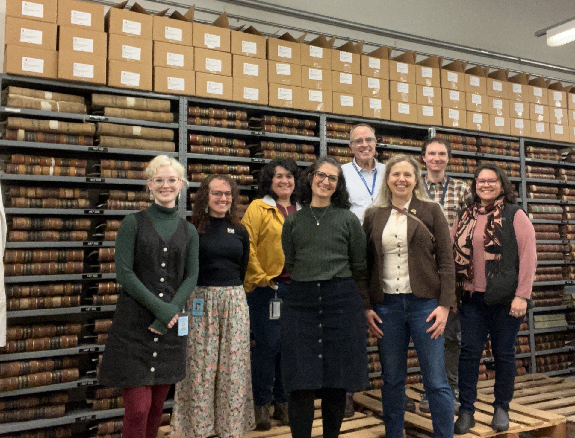 8 staffers posing in front of shelves of old ledgers