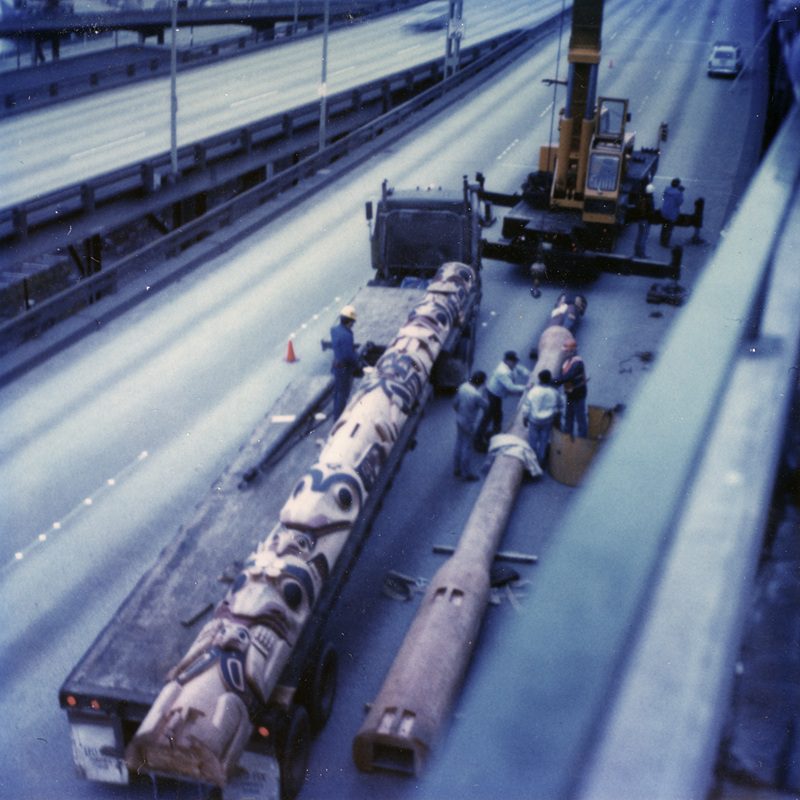 color photo of two totem poles loaded onto a flatbed truck being driven down a highway