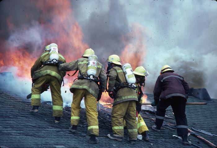 Firefighters fighting flames on roof in full gear.