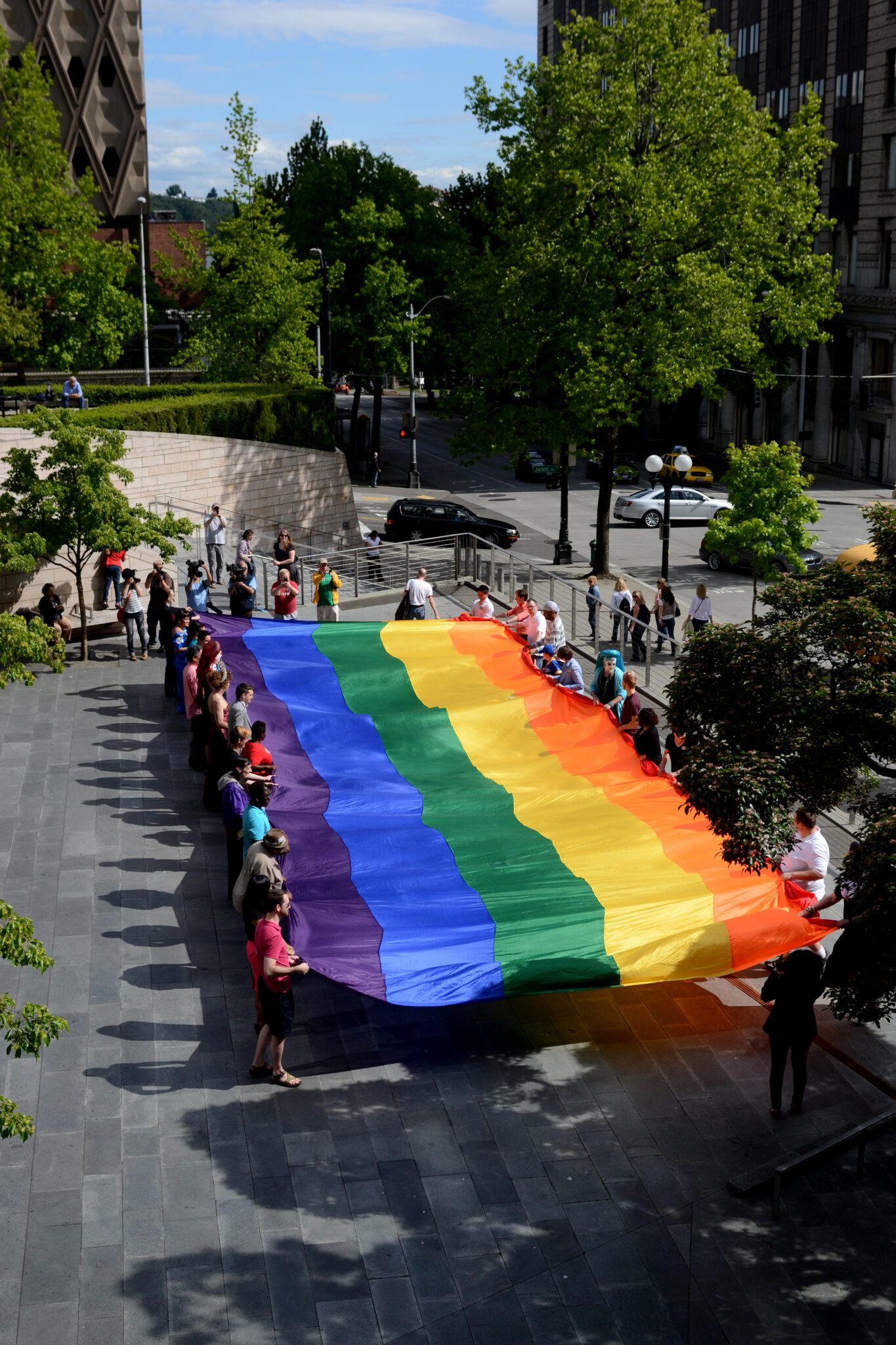 Color photo of people standing outside preparing to raise the Pride flag at City Hall in June 2013