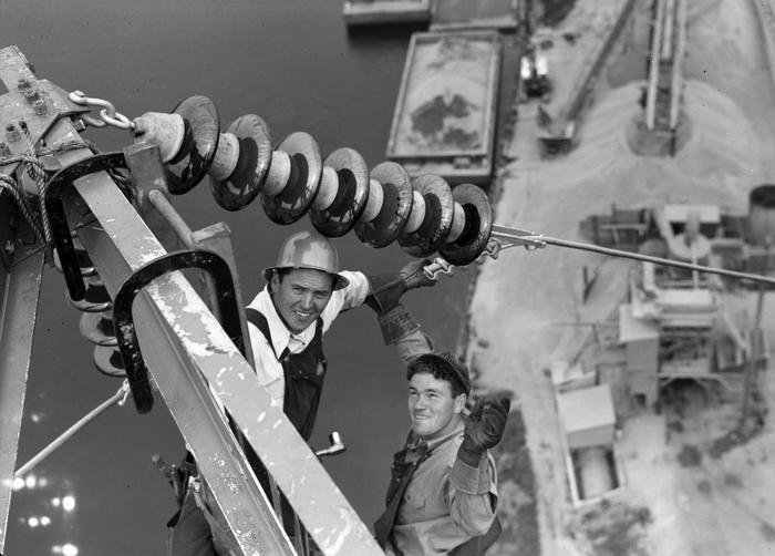 Two lineman high up on transmission line, photographed from above